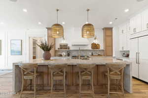 Kitchen featuring paneled refrigerator, light stone counters, a large island with sink, pendant lighting, and light hardwood / wood-style flooring