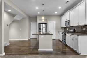 Kitchen with white cabinets, appliances with stainless steel finishes, pendant lighting, and an island with sink