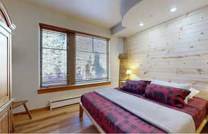 Bedroom with wood-type flooring, baseboard heating, and wooden walls