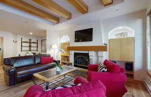 Living room featuring baseboard heating, a healthy amount of sunlight, beam ceiling, and light wood-type flooring