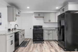 Kitchen with black appliances, sink, light hardwood / wood-style flooring, gray cabinets, and light stone countertops