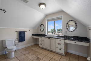 Bathroom featuring vanity, tile patterned floors, vaulted ceiling, toilet, and a textured ceiling