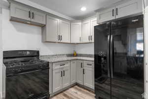 Kitchen featuring gray cabinetry, light stone counters, black appliances, and light wood-type flooring