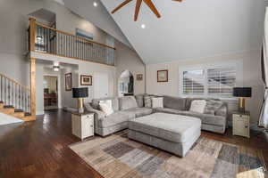 Living room with ceiling fan, a fireplace, high vaulted ceiling, and dark wood-type flooring