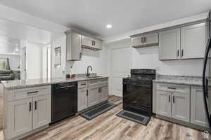 Kitchen featuring light stone countertops, gray cabinetry, sink, black appliances, and hardwood / wood-style floors