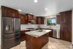 Kitchen featuring light tile patterned flooring, sink, light stone countertops, appliances with stainless steel finishes, and a kitchen island