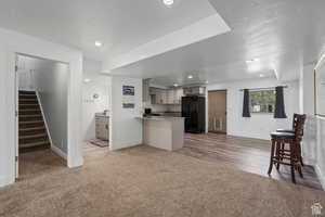 Kitchen featuring carpet, black refrigerator with ice dispenser, kitchen peninsula, light stone counters, and white cabinetry