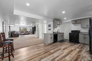 Kitchen featuring carpet, sink, gray cabinetry, and black appliances