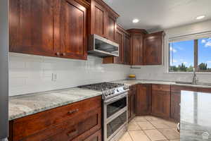 Kitchen featuring light stone countertops, sink, decorative backsplash, light tile patterned flooring, and appliances with stainless steel finishes