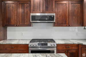 Kitchen featuring appliances with stainless steel finishes, tasteful backsplash, and light stone counters