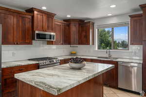 Kitchen with sink, light stone countertops, light tile patterned floors, appliances with stainless steel finishes, and a kitchen island