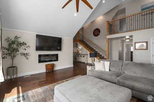 Living room with ceiling fan, dark wood-type flooring, and high vaulted ceiling