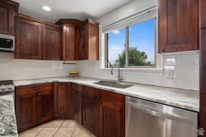 Kitchen with backsplash, light stone countertops, sink, and appliances with stainless steel finishes