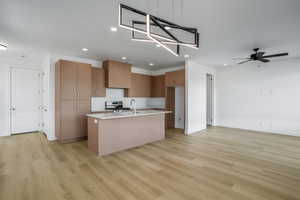 Kitchen with ceiling fan, stainless steel gas range, pendant lighting, light hardwood / wood-style floors, and a kitchen island with sink