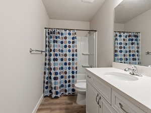 Full bathroom featuring vanity, shower / bath combo, hardwood / wood-style flooring, toilet, and a textured ceiling