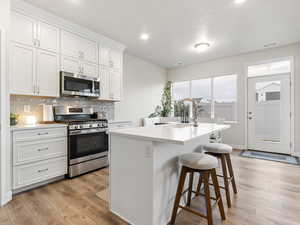 Kitchen with backsplash, a kitchen island with sink, sink, appliances with stainless steel finishes, and white cabinetry