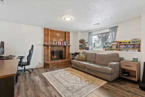 Living room featuring hardwood / wood-style floors, a textured ceiling, and a brick fireplace