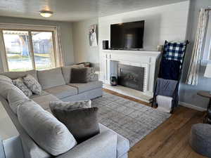 Living room with hardwood / wood-style floors, a textured ceiling, and a brick fireplace