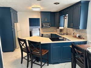 Kitchen with kitchen peninsula, stainless steel appliances, sink, blue cabinetry, and washing machine and dryer