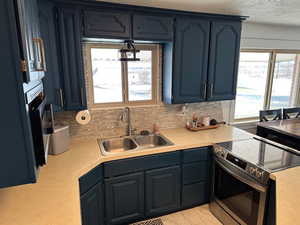 Kitchen with sink, backsplash, blue cabinets, and electric stove