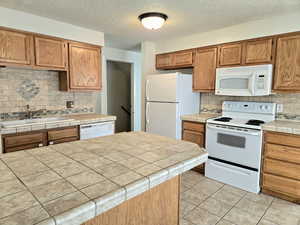 Kitchen featuring white appliances, sink, tasteful backsplash, tile counters, and light tile patterned flooring