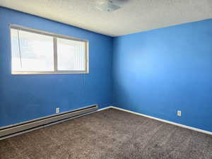 Carpeted empty room featuring a textured ceiling and a baseboard heating unit