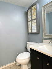 Bathroom featuring tile patterned flooring, vanity, toilet, and a textured ceiling