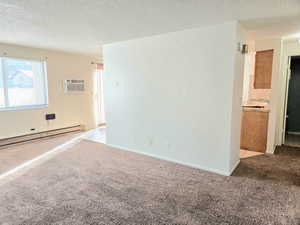 Empty room featuring light carpet, a textured ceiling, an AC wall unit, and baseboard heating