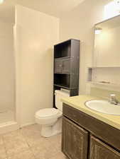 Bathroom with tiled shower, vanity, tile patterned flooring, and toilet