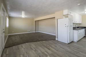 Kitchen featuring a textured ceiling, sink, light hardwood / wood-style flooring, white cabinets, and white fridge