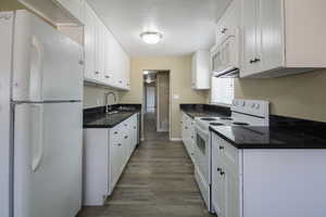 Kitchen featuring sink, white cabinets, dark hardwood / wood-style floors, and white appliances