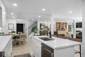 Kitchen with dishwasher, white cabinets, a center island with sink, sink, and light hardwood / wood-style flooring