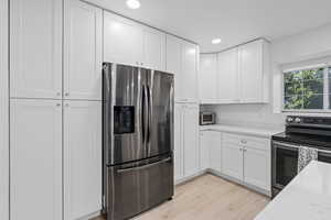 Kitchen with light stone countertops, stainless steel appliances, white cabinetry, and light hardwood / wood-style floors