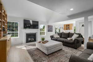 Living room featuring light hardwood / wood-style flooring, a high end fireplace, a healthy amount of sunlight, and vaulted ceiling