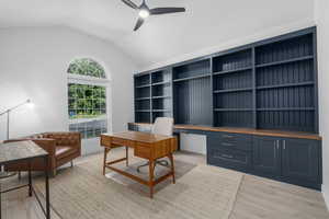 Office featuring ceiling fan, built in desk, vaulted ceiling, and light wood-type flooring