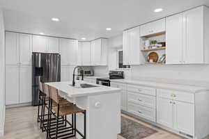 Kitchen with a kitchen bar, appliances with stainless steel finishes, a kitchen island with sink, sink, and white cabinetry