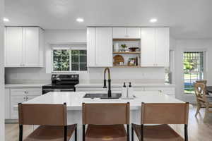 Kitchen featuring stainless steel range with electric stovetop, sink, an island with sink, a kitchen bar, and white cabinetry