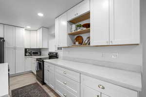 Kitchen with white cabinets, electric range, light stone countertops, light wood-type flooring, and fridge