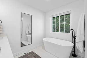 Bathroom featuring tile patterned flooring, vanity, and a tub to relax in