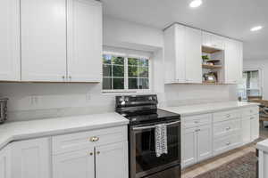 Kitchen with white cabinets, light hardwood / wood-style floors, stainless steel electric range oven, and a wealth of natural light