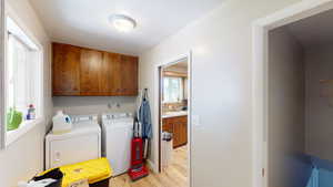 Washroom with washing machine and dryer, sink, cabinets, and light wood-type flooring