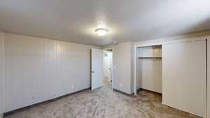 Unfurnished bedroom with light carpet, a closet, wood walls, and a textured ceiling