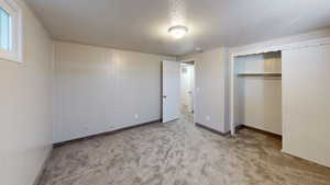 Unfurnished bedroom featuring wooden walls, a closet, light carpet, and a textured ceiling