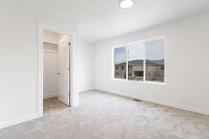 Unfurnished bedroom featuring a walk in closet, light carpet, and a closet