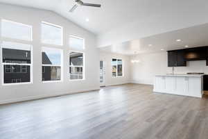 Unfurnished living room with ceiling fan with notable chandelier, light wood-type flooring, sink, and lofted ceiling