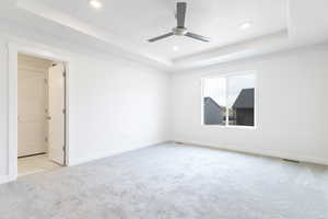 Carpeted empty room featuring ceiling fan and a tray ceiling