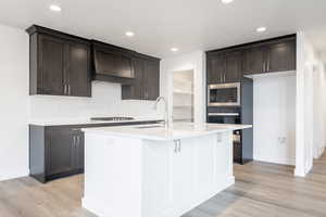 Kitchen with stainless steel microwave, light hardwood / wood-style flooring, black oven, a kitchen island with sink, and custom exhaust hood