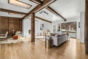 Living room featuring lofted ceiling with beams, a fireplace, light hardwood / wood-style floors, and a textured ceiling