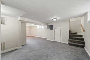 Basement with electric panel, a textured ceiling, and dark colored carpet