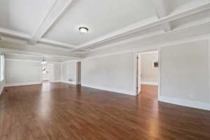 Unfurnished living room featuring beam ceiling, dark wood-type flooring, and ornamental molding